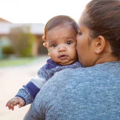 An Indigenous woman kisses a baby looking over her shoulder.